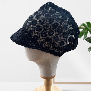 May include: A black lace hat with a floral design. The hat is on a wooden display stand.