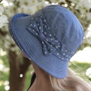 May include: A blue denim sun hat with a white polka dot bow. The hat has a wide brim and is made of a soft, comfortable fabric.