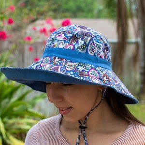 May include: A wide-brimmed sun hat with a blue paisley print and a blue ribbon around the crown. The hat has a chin strap.