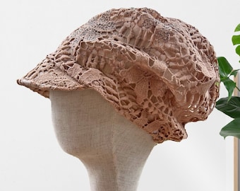 May include: A light brown crocheted hat with a floral design. The hat is displayed on a wooden mannequin head.