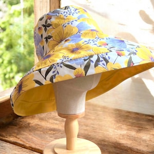 May include: A wide-brimmed sun hat with a yellow and blue floral print. The hat is made of fabric and has a wide brim that provides shade from the sun.