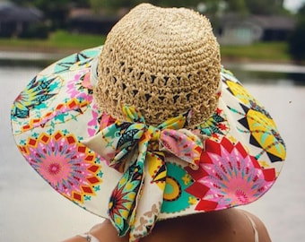 May include: A wide-brimmed sun hat with a straw crown and a colorful floral fabric brim. The hat has a large bow at the back.