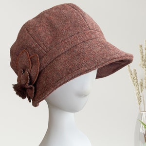May include: A brown felt newsboy cap with a flower accent. The cap has a wide brim and a slightly rounded crown.