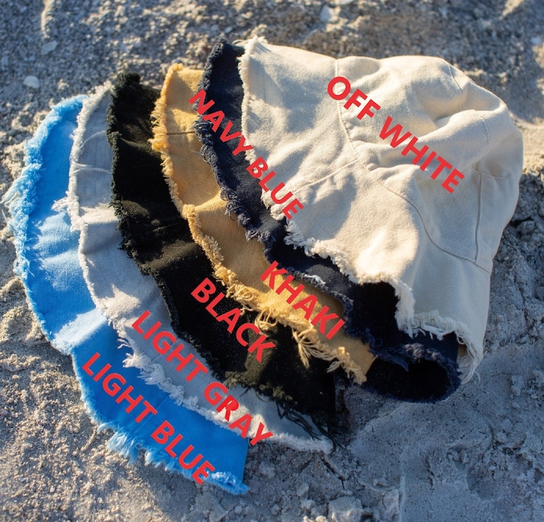 May include: A stack of six bucket hats in different colors, including off white, navy blue, khaki, black, light gray, and light blue. The hats have a frayed edge.