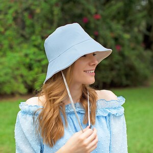 May include: A light blue bucket hat with a white ribbon tied under the chin. The hat is made of a soft, lightweight fabric and has a wide brim.