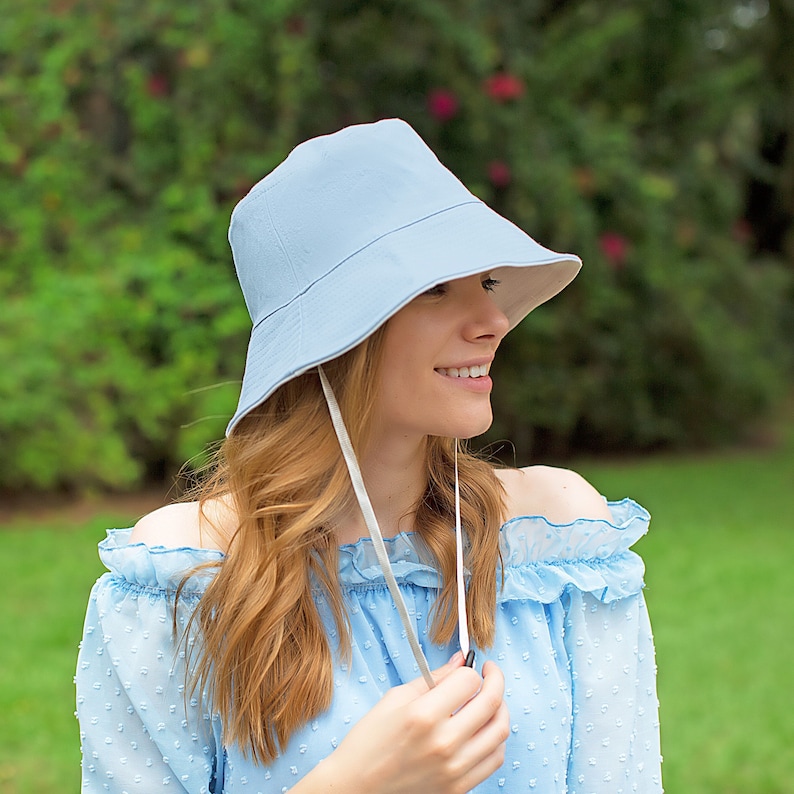 May include: A light blue bucket hat with a white ribbon tied under the chin. The hat is made of a soft, lightweight fabric and has a wide brim.