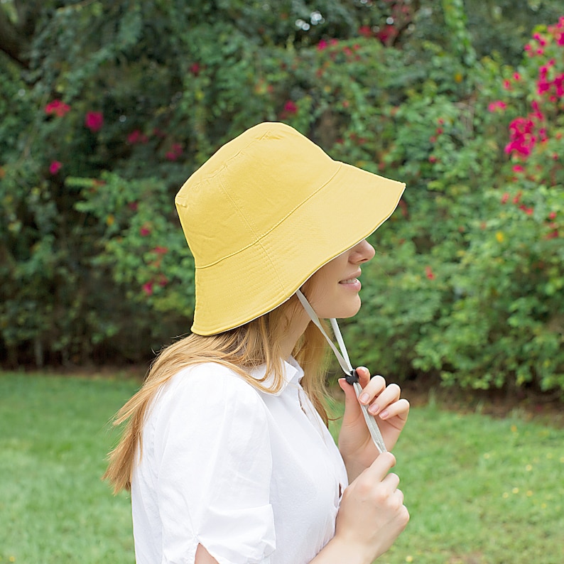 May include: A yellow bucket hat with a white chin strap. The hat is made of a soft, lightweight fabric and has a wide brim.