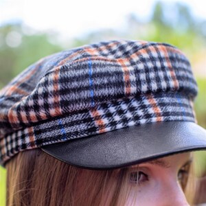 May include: A black, white, and orange plaid newsboy cap with a black leather brim.