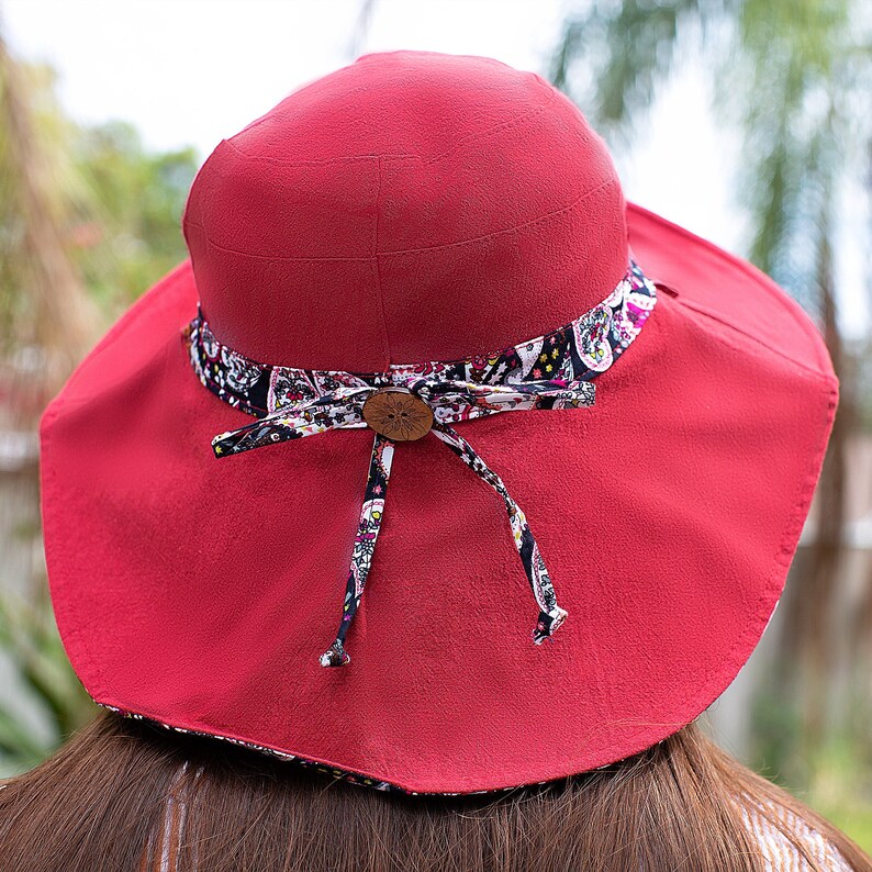 May include: A red sun hat with a wide brim and a patterned fabric band. The band has a wooden button in the center.