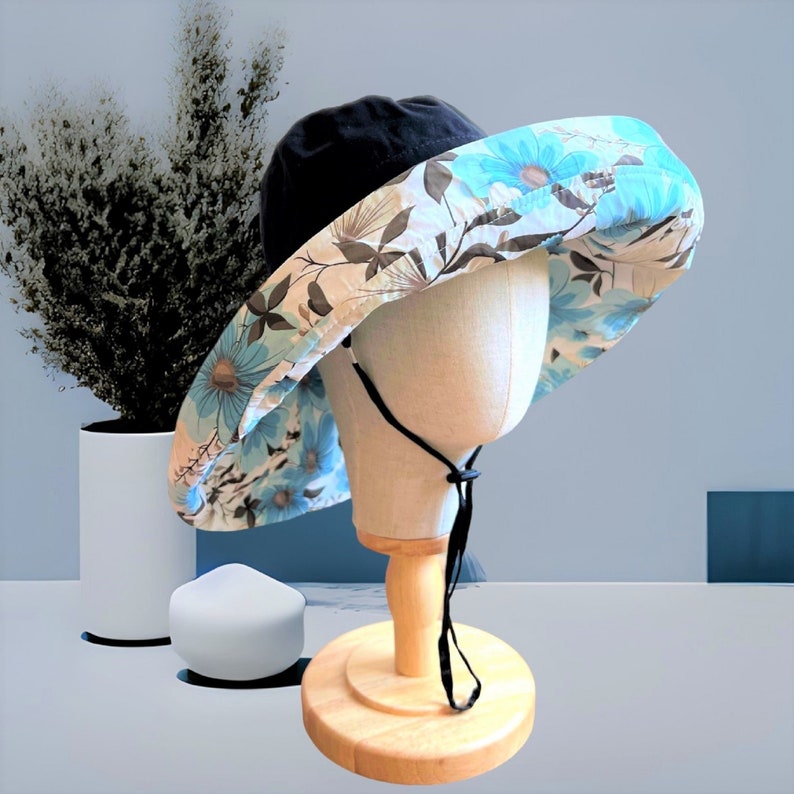 May include: A wide-brimmed sun hat with a black crown and a floral print in shades of blue, white, and brown. The hat has a black chin strap.