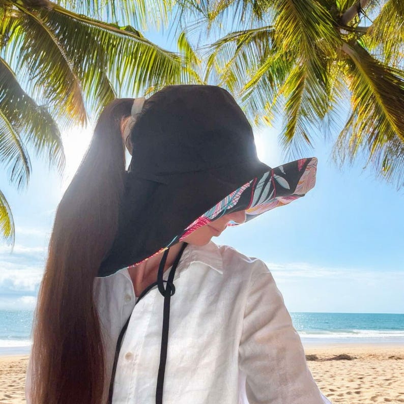 May include: A black sun hat with a floral print lining. The hat has a wide brim and a chin strap. The hat is being worn by a person with long brown hair.