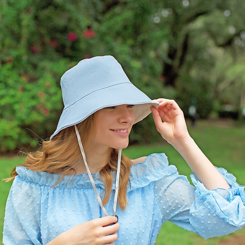 May include: A light blue bucket hat with a white chin strap. The hat is made of a soft, lightweight fabric and has a wide brim.