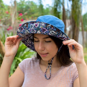 Pode incluir: Uma mulher usando um chap&eacute;u de sol azul com uma ampla aba e um padr&atilde;o floral. O chap&eacute;u tem uma correia de queixo e &eacute; amarrado na parte de tr&aacute;s do pesco&ccedil;o.