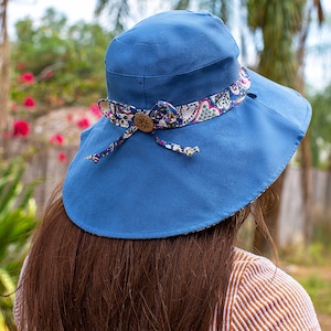 May include: A blue sun hat with a wide brim and a floral patterned ribbon. The hat is tied at the back with a bow.