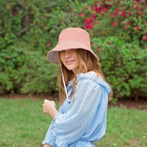 May include: A woman wearing a light blue, polka dot, off-the-shoulder blouse with a light brown bucket hat.