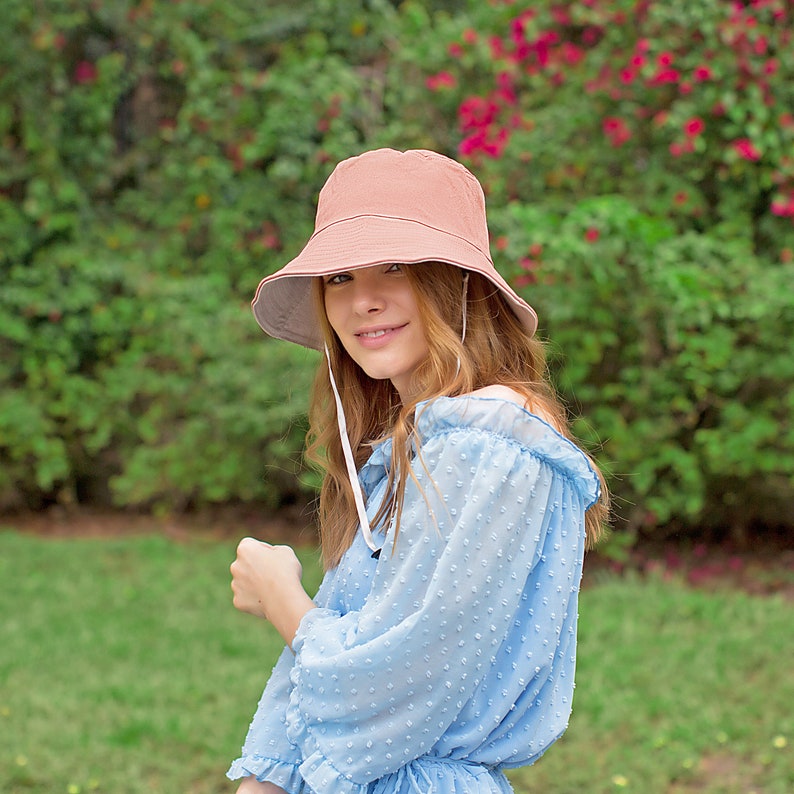May include: A woman wearing a light blue, polka dot, off-the-shoulder blouse with a light brown bucket hat.