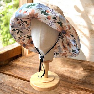 May include: A wide-brimmed sun hat with a floral print in shades of blue, white, and orange. The hat has a black adjustable chin strap.