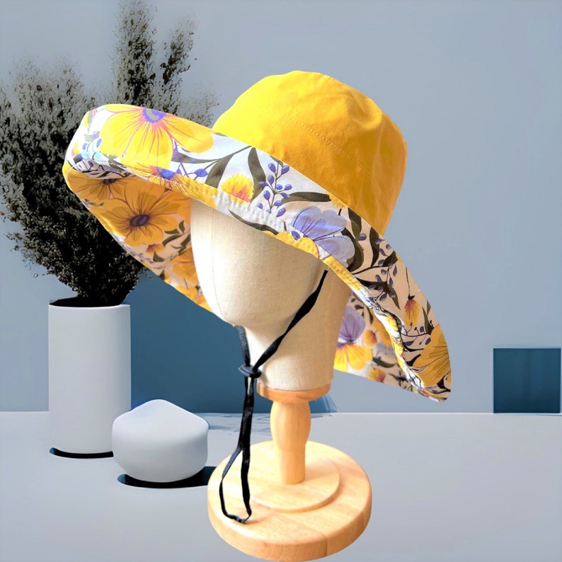 May include: A yellow sun hat with a floral print lining. The hat has a wide brim and a black ribbon tie.
