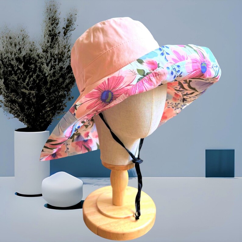 May include: A pink and floral sun hat with a black chin strap. The hat is on a wooden display stand.