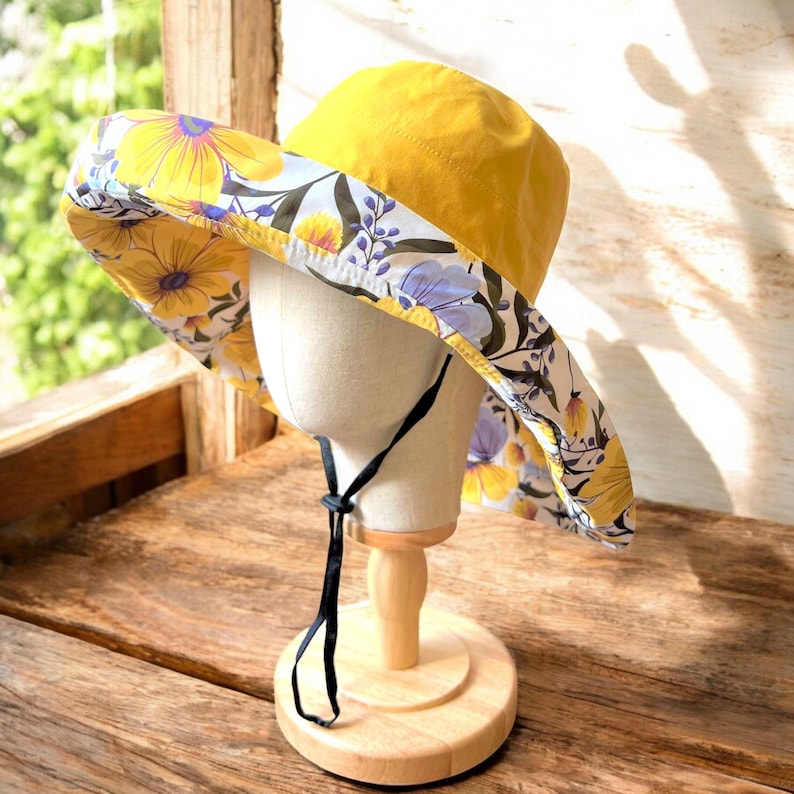 May include: A yellow sun hat with a floral print lining. The hat has a wide brim and a black tie.