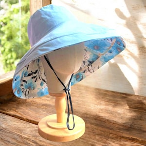 May include: A light blue sun hat with a floral print lining. The hat has a wide brim and a black tie.