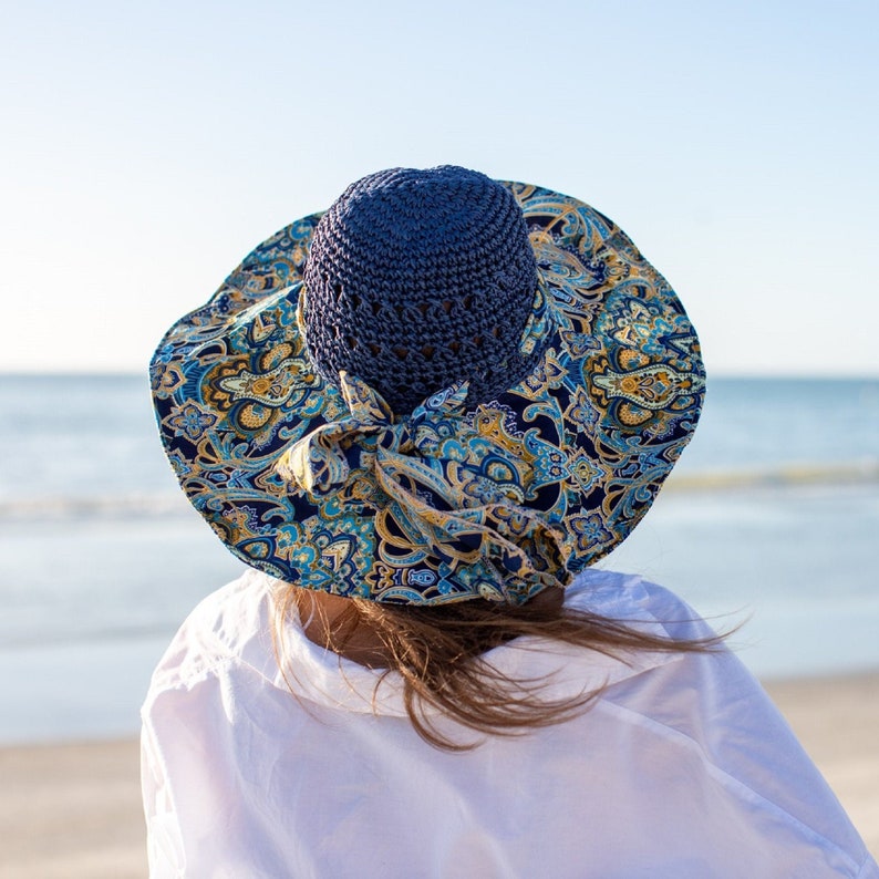 K&ouml;nnte beinhalten: Eine Frau tr&auml;gt ein wei&szlig;es Hemd und einen blauen und gelben gemusterten Sonnenhut mit einer blauen H&auml;kelkrone.