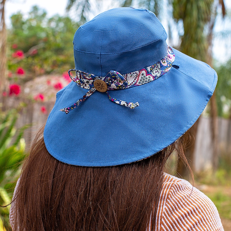 Pode incluir: Um chap&eacute;u de sol azul com aba larga e uma fita com padr&atilde;o floral. O chap&eacute;u &eacute; amarrado na parte de tr&aacute;s com um la&ccedil;o.