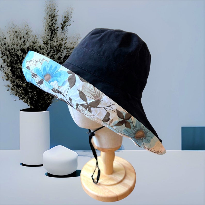 May include: A black sun hat with a wide brim and a floral print lining. The hat is made of a soft, lightweight fabric and has a black ribbon tie.