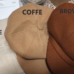 May include: Three newsboy-style hats in beige, coffee, and brown. The hats have a rounded crown and a small, stiff brim. The word "BEIGE" is printed on the beige hat, "COFFE" on the coffee hat, and "BROWN" on the brown hat.