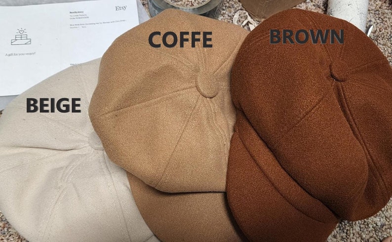 May include: Three newsboy-style hats in beige, coffee, and brown. The hats have a rounded crown and a small, stiff brim. The word "BEIGE" is printed on the beige hat, "COFFE" on the coffee hat, and "BROWN" on the brown hat.