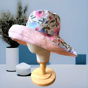 May include: A pink and white floral sun hat with a wide brim. The hat is made of fabric and has a pink underside.