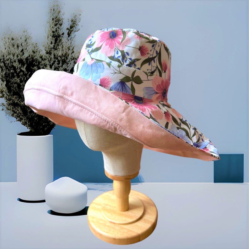May include: A pink and white floral sun hat with a wide brim. The hat is made of fabric and has a pink underside.