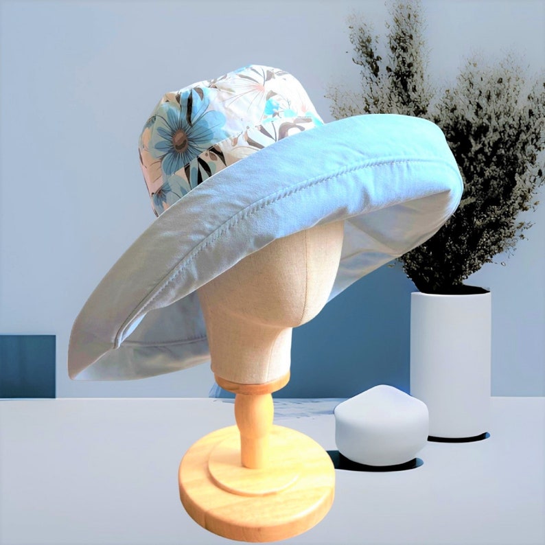May include: A light blue sun hat with a floral print on the crown. The hat is on a wooden display stand.