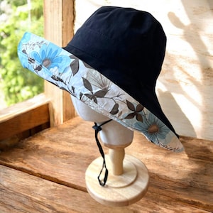 May include: A black sun hat with a wide brim and a floral print on the underside. The brim is turned up on one side.