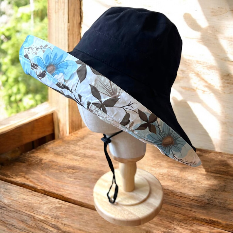 May include: A black sun hat with a wide brim and a floral print on the underside. The brim is turned up on one side.