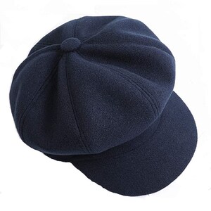 May include: A navy blue newsboy cap with a rounded crown and a short, curved peak. The cap features a button detail at the top and is made from a soft, textured fabric. A classic hat suitable for various occasions.