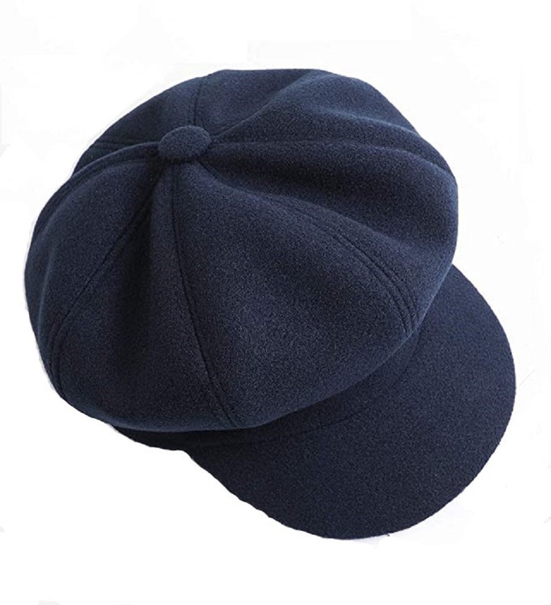 May include: A navy blue newsboy cap with a rounded crown and a short, curved peak. The cap features a button detail at the top and is made from a soft, textured fabric. A classic hat suitable for various occasions.