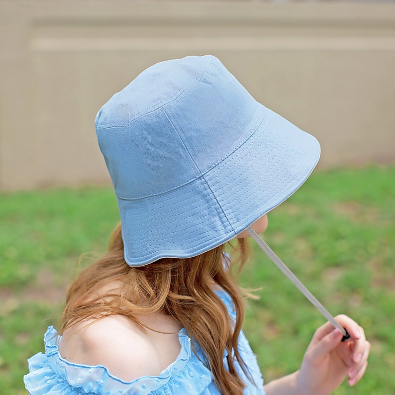May include: A light blue bucket hat with a white drawstring. The hat is made of a soft, lightweight fabric and has a wide brim.