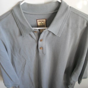May include: A light gray short-sleeved polo shirt with a button-down collar. The shirt has a Tommy Bahama logo on the left chest.