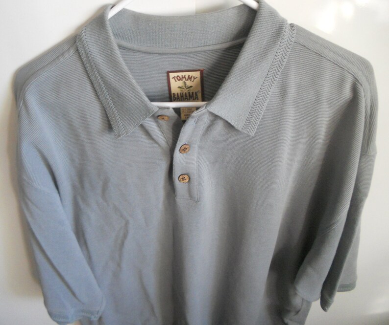 May include: A light gray short-sleeved polo shirt with a button-down collar. The shirt has a Tommy Bahama logo on the left chest.