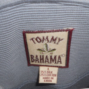 May include: A brown tag with white text that reads "TOMMY BAHAMA" with a small logo of a palm tree and a bird. The tag also has a smaller white tag attached to it that reads "L 75% SILK 25% COTTON MADE IN CHINA."