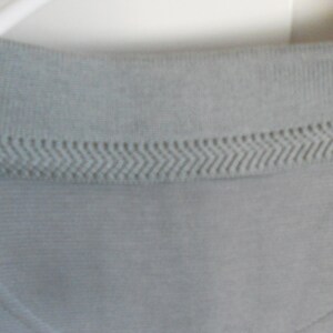 May include: A light gray polo shirt with a ribbed collar and a subtle textured pattern. The collar has a decorative stitching detail.