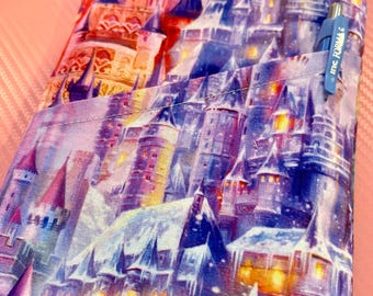 May include: An e-reader case with a vibrant castle illustration in purple, blue, and orange hues. The case includes a pocket with a blue pen and a label with the text "irishais". The case is designed to hold an e-reader, offering protection and style.