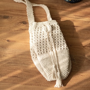 Peut inclure: Un sac en crochet blanc avec une longue bandouli&egrave;re et un pompon. Le sac est fait d'un fil &eacute;pais et textur&eacute; et a un design simple et &eacute;l&eacute;gant.