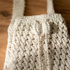 Peut inclure: Un sac en crochet blanc avec une anse nou&eacute;e. Le sac est fait d'un fil &eacute;pais et textur&eacute; et a un design simple et minimaliste.