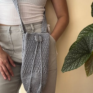 Peut inclure: Un sac &agrave; bandouli&egrave;re en crochet gris avec une fermeture &agrave; cordon et des accents de pompons.