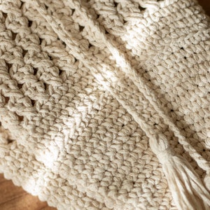 Peut inclure: Gros plan d'un sac en crochet de couleur cr&egrave;me avec un pompon. Le sac est fait d'un cordon de coton &eacute;pais et a un design simple et &eacute;l&eacute;gant.