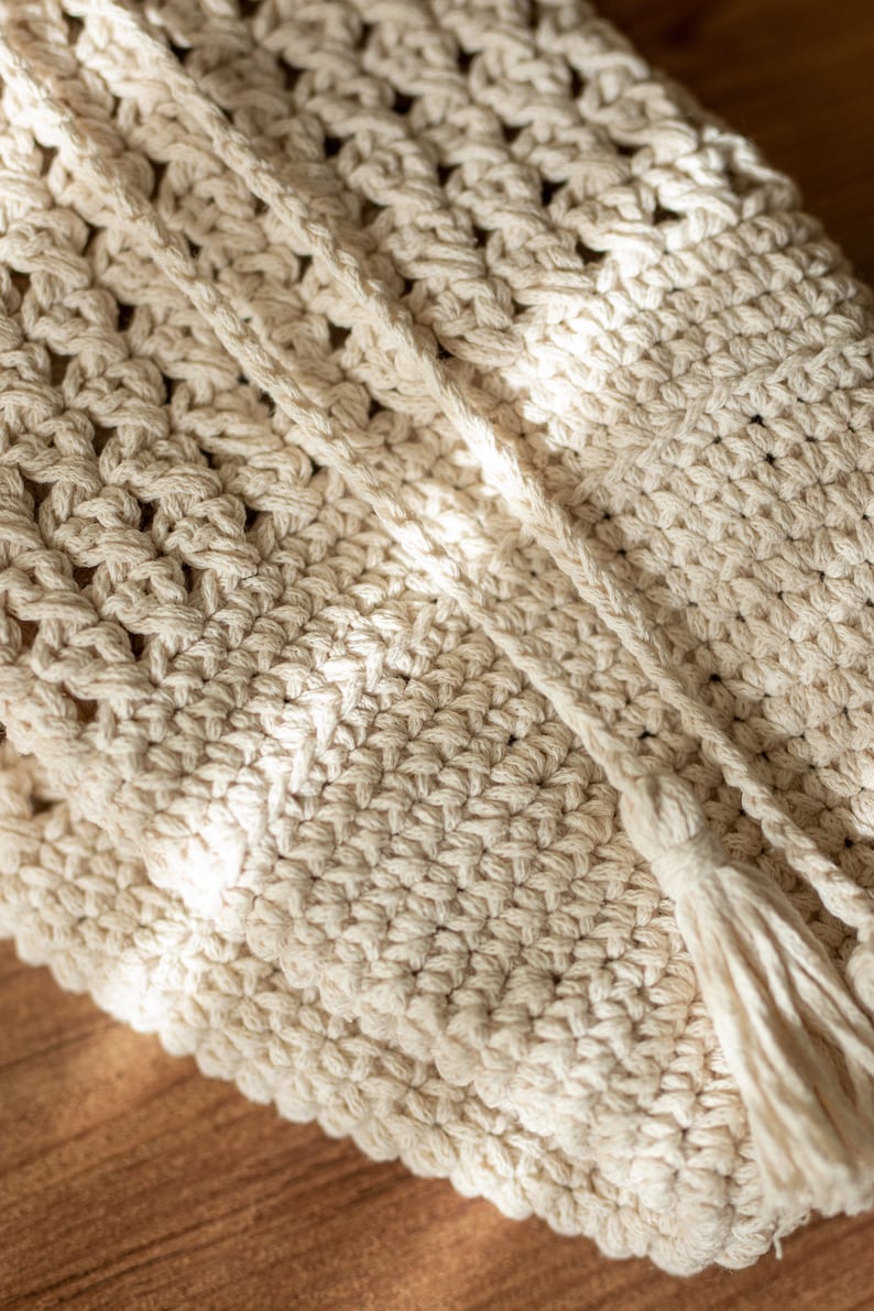Peut inclure: Gros plan d'un sac en crochet de couleur cr&egrave;me avec un pompon. Le sac est fait d'un cordon de coton &eacute;pais et a un design simple et &eacute;l&eacute;gant.