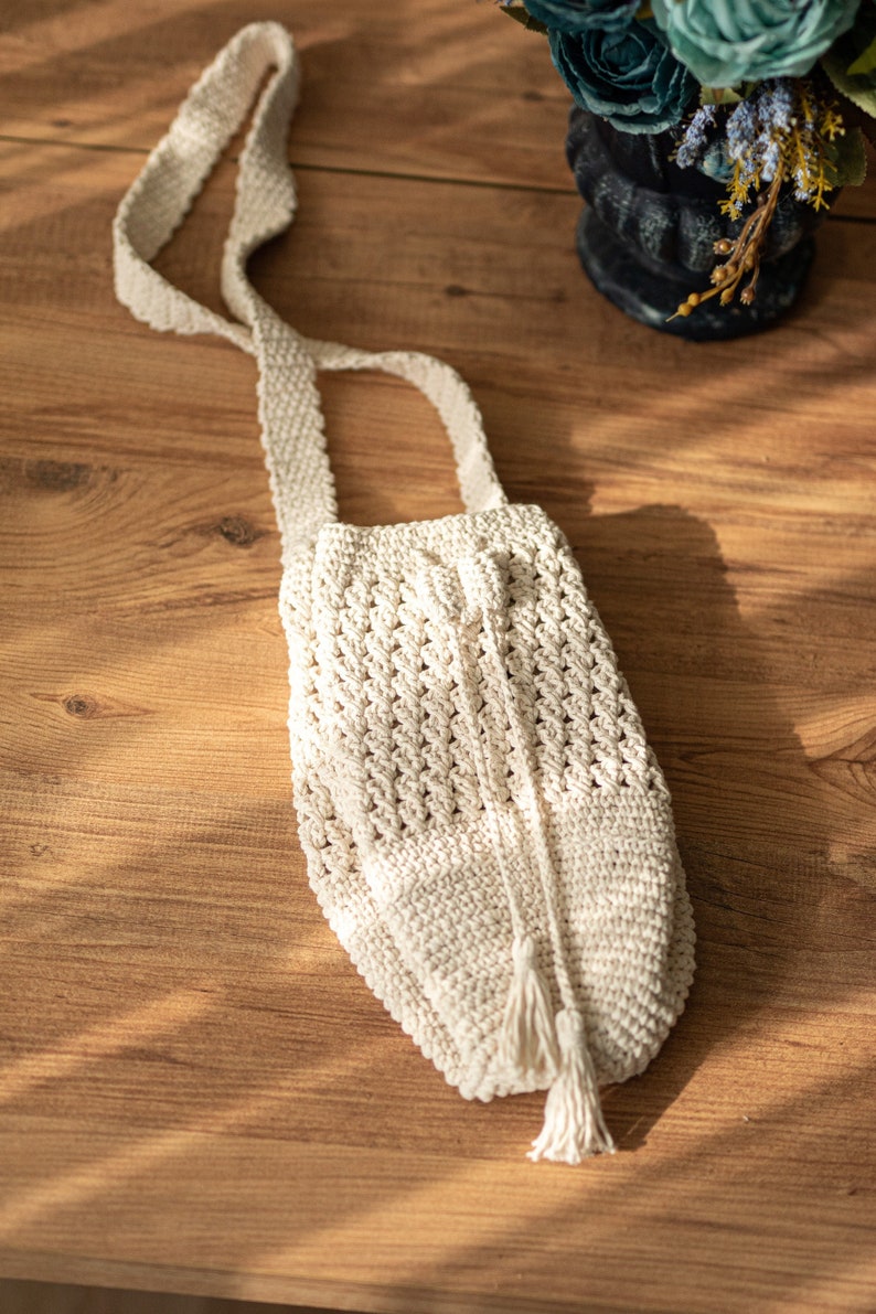 Peut inclure: Un sac en crochet blanc avec une longue bandouli&egrave;re et un pompon. Le sac est fait d'un fil &eacute;pais et textur&eacute; et a un design simple et &eacute;l&eacute;gant.