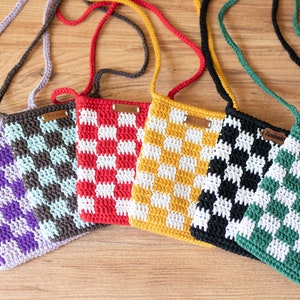 May include: Six crocheted checkerboard crossbody bags in various colors, including purple, brown, red, yellow, black, and green. Each bag has a small leather tag with the word "Handmade" on it.